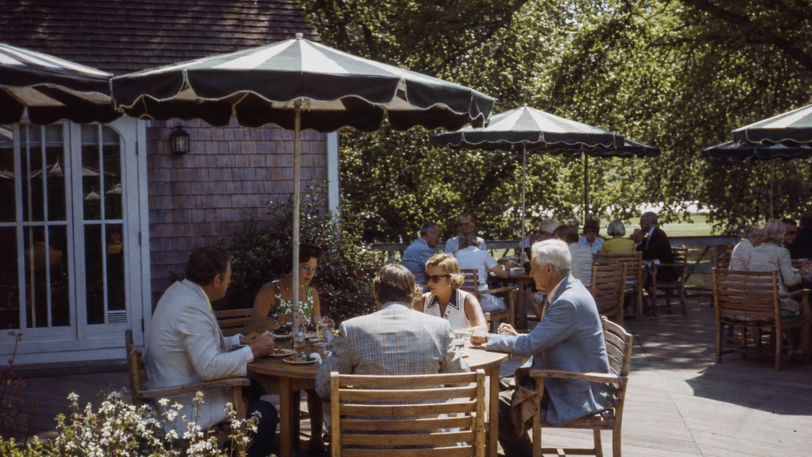 Members at lunch beneath green umbrellas on the clubhouse terrace.